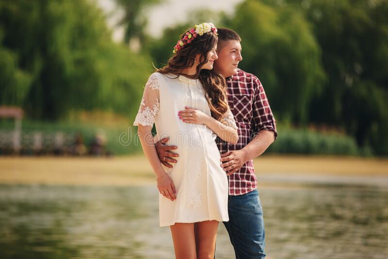 young happy romantic pregnant couple hugging nature near lake summer park pregnant women expecting baby future mom dad 180399945